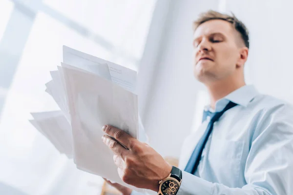 Vue en angle bas des papiers en main de l'homme d'affaires en colère sur fond flou — Photo de stock