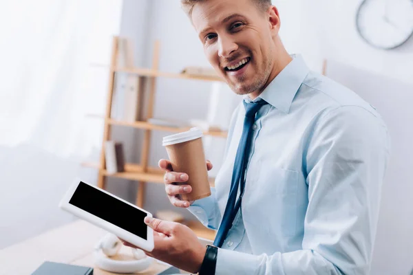 Homme d'affaires joyeux avec du café à emporter et tablette numérique regardant l'appareil photo — Photo de stock