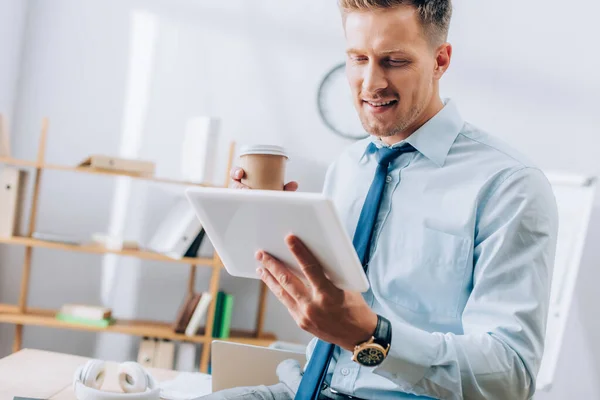 Uomo d'affari sorridente utilizzando tablet digitale mentre tiene in mano il caffè per andare — Foto stock