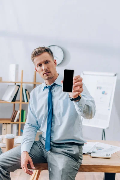 Jeune homme d'affaires montrant smartphone avec écran blanc au premier plan flou — Photo de stock