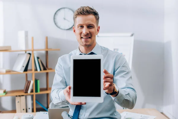 Homme d'affaires souriant montrant tablette numérique avec écran blanc au premier plan flou — Photo de stock