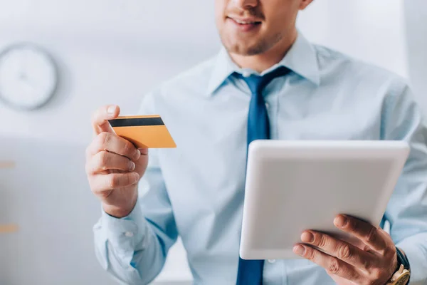 Vista recortada de tableta digital y tarjeta de crédito en manos de hombre de negocios sonriente - foto de stock