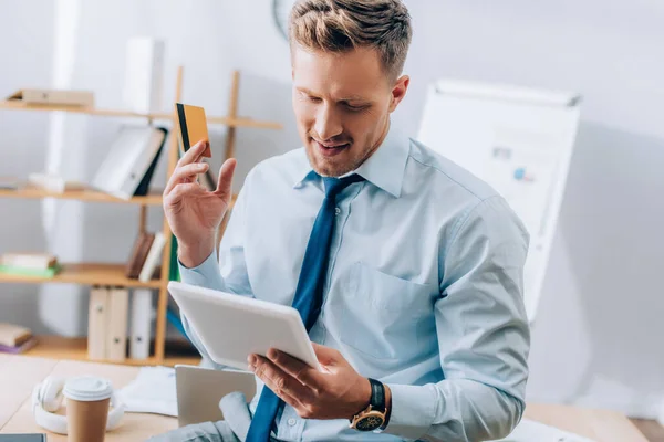 Uomo d'affari sorridente in possesso di carta di credito durante l'utilizzo di tablet digitale in ufficio — Foto stock