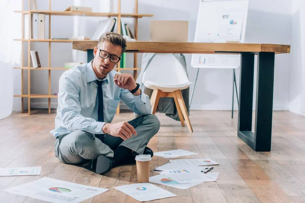 Geschäftsmann sitzt auf dem Boden neben Coffee to go und Papieren im Büro — Stockfoto