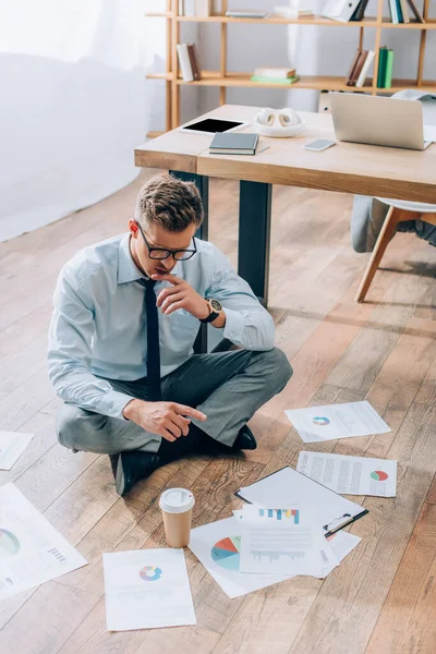 Umsichtiger Geschäftsmann schaut sich Dokumente in der Nähe von Kaffee an, um im Büro auf den Boden zu gehen — Stockfoto