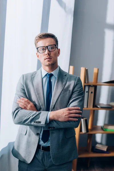 Jeune homme d'affaires en lunettes et costume regardant la caméra dans le bureau — Photo de stock