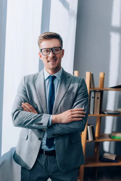 Lächelnder Geschäftsmann mit verschränkten Armen, der im Büro in die Kamera schaut — Stockfoto