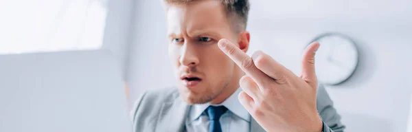 Uomo d'affari aggressivo che mostra il dito medio durante l'utilizzo di laptop in primo piano sfocato, banner — Foto stock