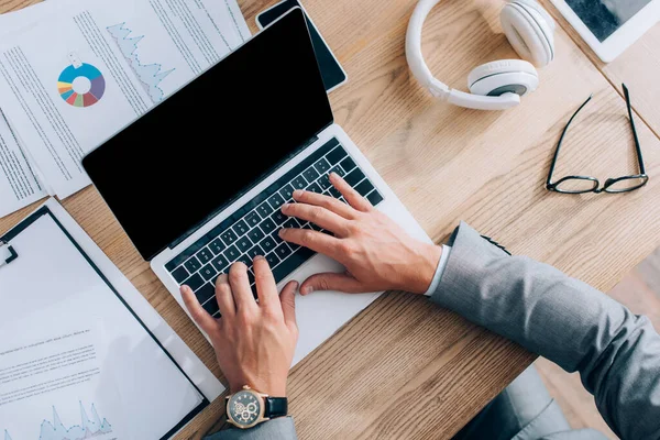 Vista superior del hombre de negocios usando el ordenador portátil con la pantalla en blanco cerca de los papeles en la mesa - foto de stock