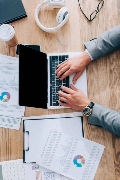 Vue du dessus de l'homme d'affaires en utilisant un ordinateur portable avec écran vierge près des documents, café à emporter et écouteurs — Photo de stock