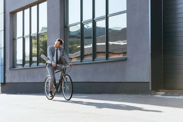 Young businessman riding bicycle near building outdoors — Stock Photo