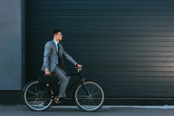 Молодий бізнесмен з портфелем їзда на велосипеді біля фасаду будівлі — стокове фото