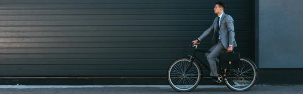 Giovane uomo d'affari che tiene la valigetta mentre va in bicicletta all'aperto, banner — Foto stock