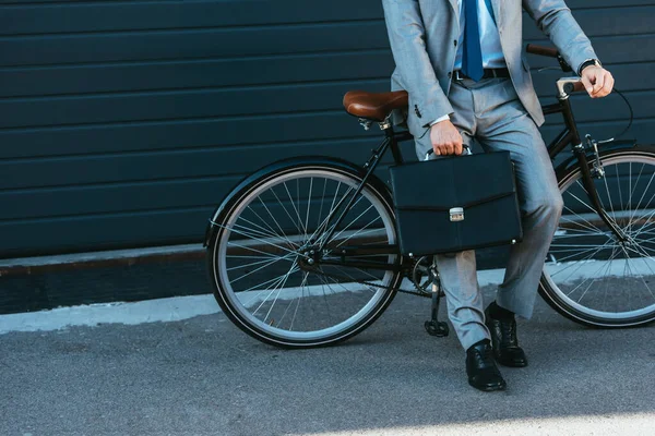 Vista cortada de homem de negócios com pasta de pé perto de bicicleta ao ar livre — Fotografia de Stock