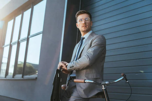 Uomo d'affari con valigetta toccante orologio da polso vicino alla bicicletta all'aperto — Foto stock