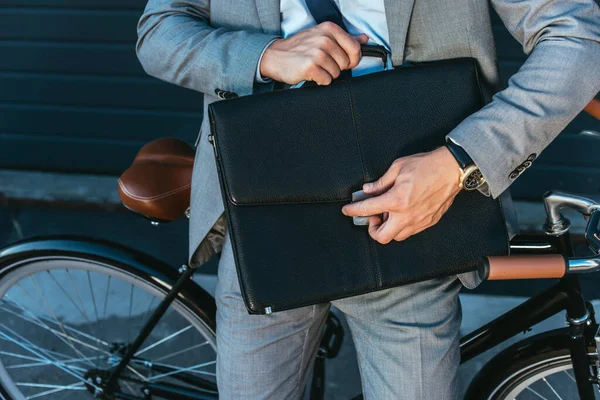 Cropped view of businessman locking briefcase beside bicycle outdoors — Stock Photo