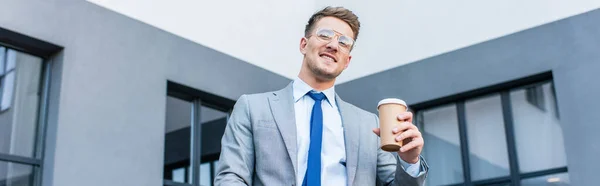 Jovem empresário sorrindo para a câmera enquanto segura café para ir ao ar livre, banner — Fotografia de Stock