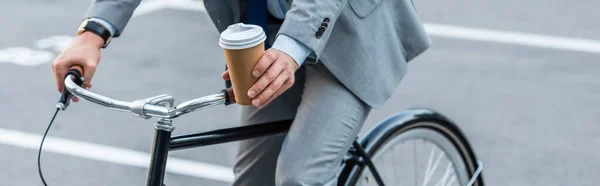 Vue recadrée de l'homme d'affaires tenant du café à emporter en vélo à l'extérieur, bannière — Photo de stock