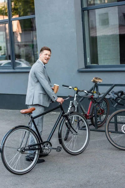 Fröhlicher Geschäftsmann mit Imbisskaffee, der in der Nähe von Fahrradabstellplätzen im Freien steht — Stockfoto