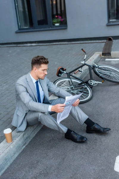 Бизнесмен читает газету, сидя рядом с вынос кофе и велосипед на открытом воздухе — стоковое фото