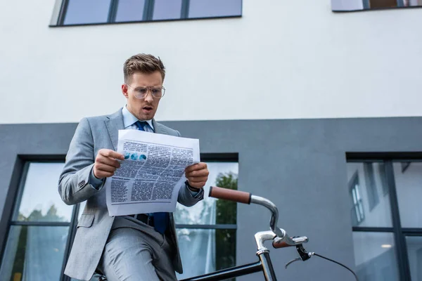 Концентрированный бизнесмен читает газету возле велосипеда на открытом воздухе — стоковое фото