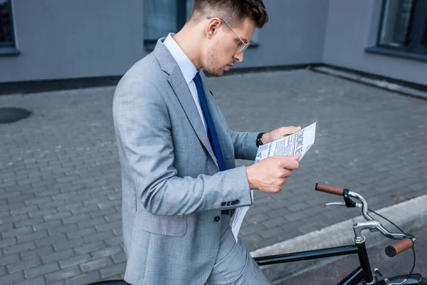 Jovem empresário lendo jornal perto de bicicleta ao ar livre — Fotografia de Stock