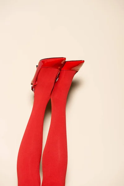 Cropped view of female legs in red tights and shoes on beige background — Stock Photo