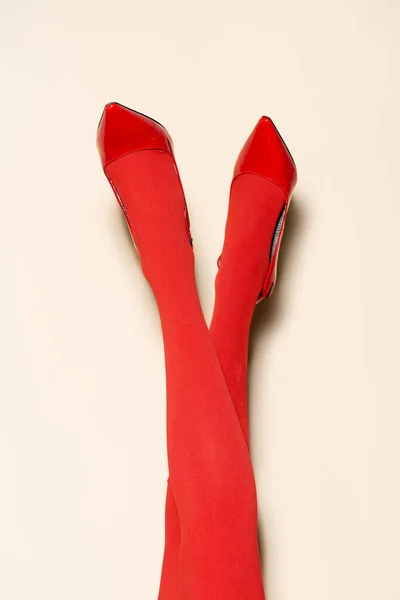 Обрезанный вид женских ног в красных колготках и обуви на бежевом фоне — стоковое фото
