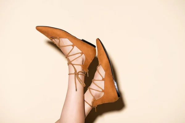 Cropped view of female legs in brown suede flat shoes on beige background — Stock Photo