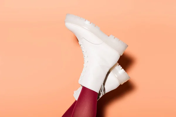 Vista cortada de pernas femininas em meias vermelhas e botas brancas no fundo de pêssego — Fotografia de Stock