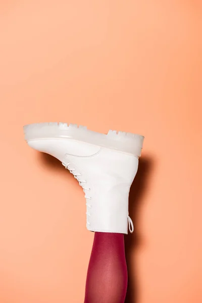 Cropped view of female leg in red tights and boots on peach background — Stock Photo