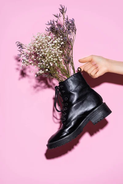 Cropped view of woman holding black boot with wildflowers on pink background — Stock Photo