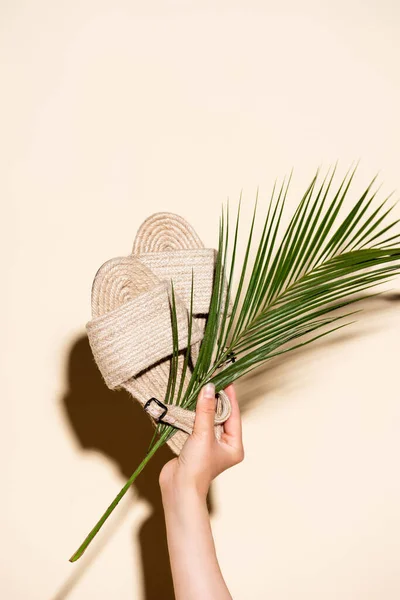 Abgeschnittene Ansicht einer Frau mit Sommer geflochtenen Sandalen und Palmblatt auf beigem Hintergrund — Stockfoto