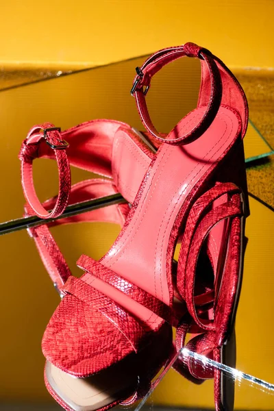 Пара элегантных розовых сандалий на каблуках из змеиной кожи на зеркальной поверхности — стоковое фото