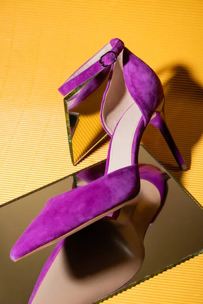 Elegante scarpa con tacco in camoscio viola su specchio su sfondo giallo — Foto stock