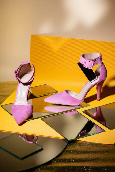 Элегантные фиолетовые замшевые туфли на каблуках на зеркале и желтой бумаге — стоковое фото