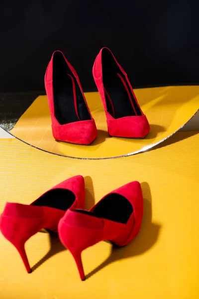 Elegant red suede heeled shoes near mirror on yellow surface — Stock Photo