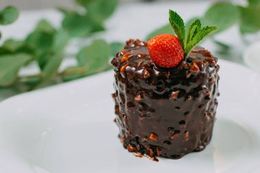 Fındıklı çikolatalı pasta, çilek ve mermer bir masada beyaz bir tabakta nane şekeri.