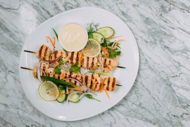 Tavuklu kebap, beyaz bir tabakta, mermer bir masada.