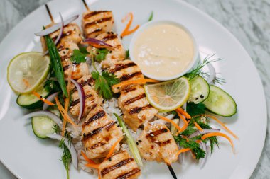 Tavuklu kebap, beyaz bir tabakta, mermer bir masada.