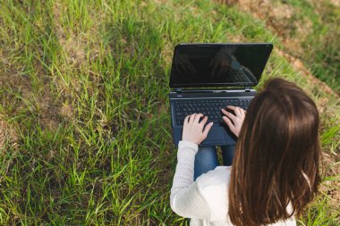 Genç iş kadını ya da boş boş ekran monitör üzerinde yeşil arka plan açık havada çalışan alan Yayilim elinde ile dizüstü bilgisayar kullanarak çimenlerin üzerinde oturan öğrenci. Mobil ofis yaşam kavramı. Arkadan Görünüm