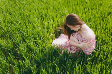 Genç sevimli kadın kapalı gözler ile ihale ve hafif desenli elbise eller katlanmış güneşli hava alanında yeşil arka plan üzerinde dinlenme tutan çimenlerin üzerinde oturan kafasına indirdi. Yaşam tarzı kavramı