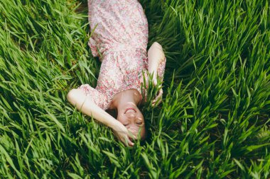 Işık genç gülümseyen kadın elbise eller baş alanındaki güneşli havalarda parlak yeşil arka plan üzerinde dinlenme kadar seyir yakınındaki tutmak çim üzerinde yalan desenli. Bahar doğa. Yaşam tarzı, eğlence kavramı