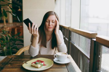 Yalnız fincan kapuçino, kafede masada oturan genç kadın kek, restoranda serbest zaman sırasında rahatlatıcı. Dinlenme kafede olan genç kadın cep telefonda konuşurken. Yaşam tarzı kavramı