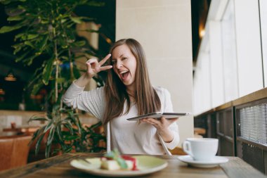 Yalnız büyük kahve dükkanında tablo penceresinde yakınındaki kapuçino, bardak ile oturan kadın kek, restoranda serbest zaman sırasında rahatlatıcı. Pc tablet bilgisayar dinlenme kafede çalışan erkek. Yaşam tarzı kavramı