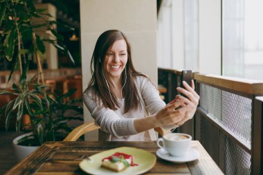 Yalnız fincan kapuçino, kafede masada oturan genç kadın kek, restoranda serbest zaman sırasında rahatlatıcı. Genç selfie cep telefonu, yapıyor kadın cafede bekletin. Yaşam tarzı kavramı