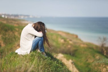 Alçaltılmış kafasından hafif rahat kıyafetler el baş suya yakın yakınında yeşil alan arka plan üzerinde tutarak çimenlerin üzerinde oturan genç esmer kadın. Güzel manzara. Yaşam tarzı, eğlence kavramı.