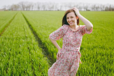 Genç esmer gülümseyen baş alanındaki güneşli havalarda yeşil arka plan üzerinde yürüme. yakınındaki el tutmak hafif desenli elbiseli güzel kadın rahat. Güzel manzara. Yaşam tarzı, eğlence kavramı