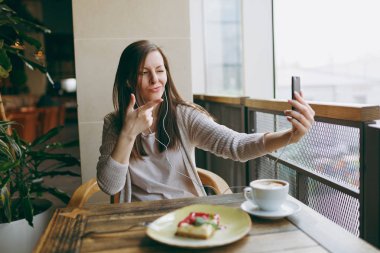 Yalnız fincan kapuçino, kafede masada oturan genç kadın kek, restoranda serbest zaman sırasında rahatlatıcı. Genç selfie cep telefonu, yapıyor kadın cafede bekletin. Yaşam tarzı kavramı