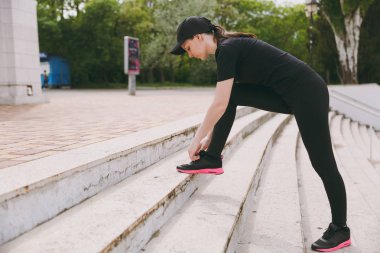 Genç atletik güzel esmer kız siyah üniforma ve cap city Park açık havada merdivenlerde bağlama ayakkabı bağcığı çalıştırmadan önce ısınma spor egzersizleri, yapıyor. Fitness, sağlıklı yaşam konsepti